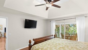 A bedroom with a bed, a ceiling fan, a TV, and a balcony with chairs. - Palm Paradise- Charming Island Bungalow in Downtown Sanibel (Sanibel)
