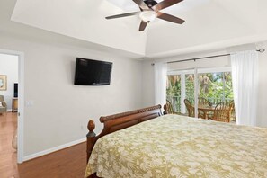 Un dormitorio con cama, ventilador de techo, televisor y balcón con sillas.