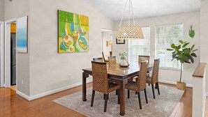 A dining area with a wooden table and wicker chairs, a hanging light fixture, and a large abstract painting on the wall. - Palm Paradise- Charming Island Bungalow in Downtown Sanibel (Sanibel)
