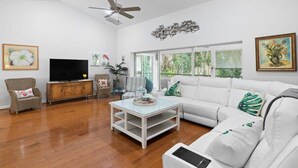 A living room with a white sofa, a television, a coffee table, and a ceiling fan. - Palm Paradise- Charming Island Bungalow in Downtown Sanibel (Sanibel)