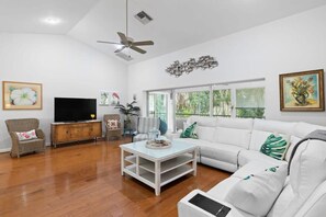 Un salón con un sofá blanco, televisor, mesa de centro y ventilador de techo.