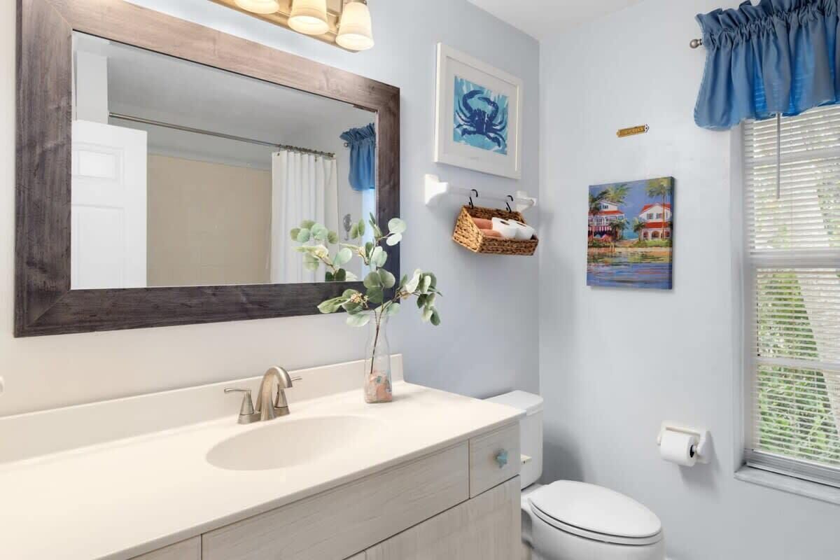 Un bagno con uno specchio grande, un lavandino, un water e una finestra con persiane.