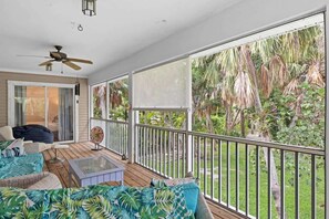 A covered balcony with a ceiling fan, a glass table, and a sofa with tropical cushions. - Palm Paradise- Charming Island Bungalow in Downtown Sanibel (Sanibel)