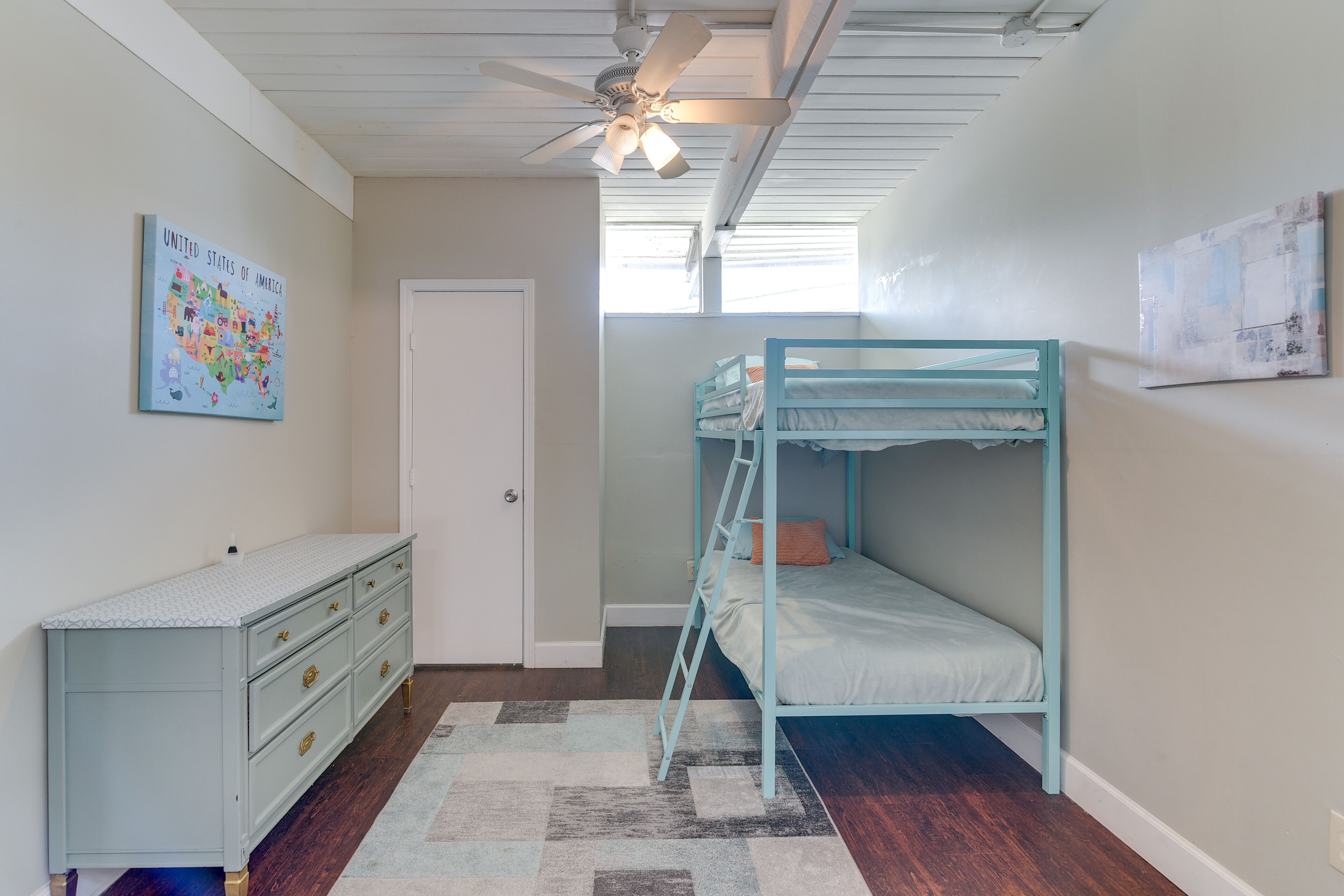 A bedroom with a bunk bed, a dresser, a ceiling fan, and a map of the United States on the wall.