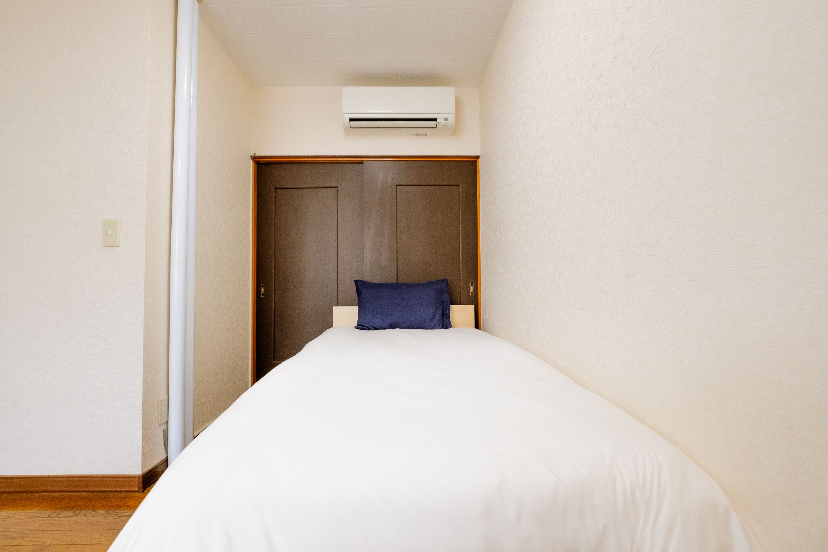 Une chambre avec un lit, une armoire en bois et un climatiseur fixé au mur.
