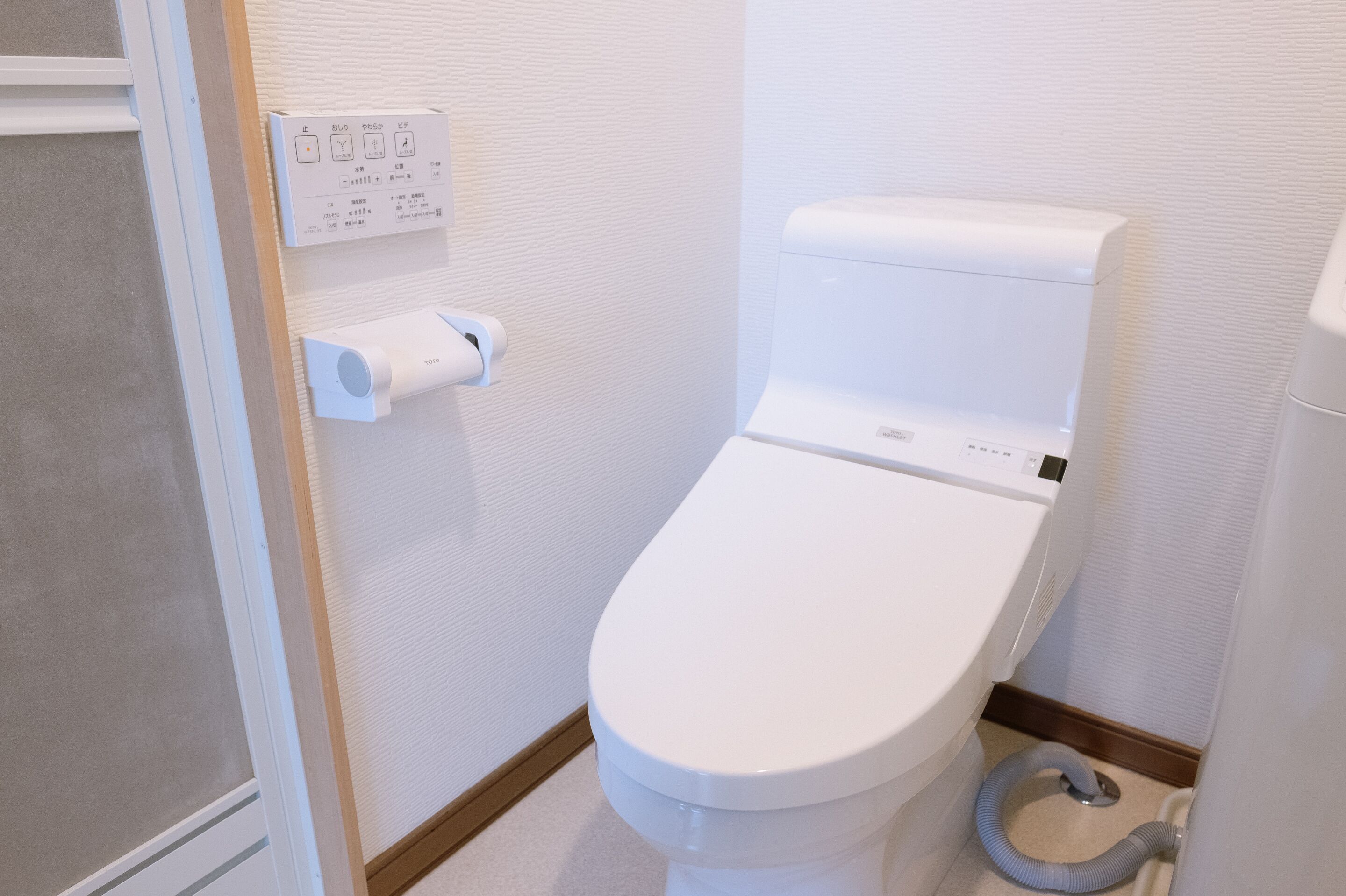 A modern bathroom with a toilet, a hand dryer, and a control panel on the wall.