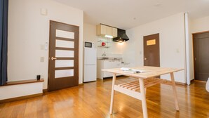 A modern kitchen with white cabinets, a microwave, and a stove. There is a wooden table with a white cloth in the living area. - Furano Zone Ski Condo (Furano)