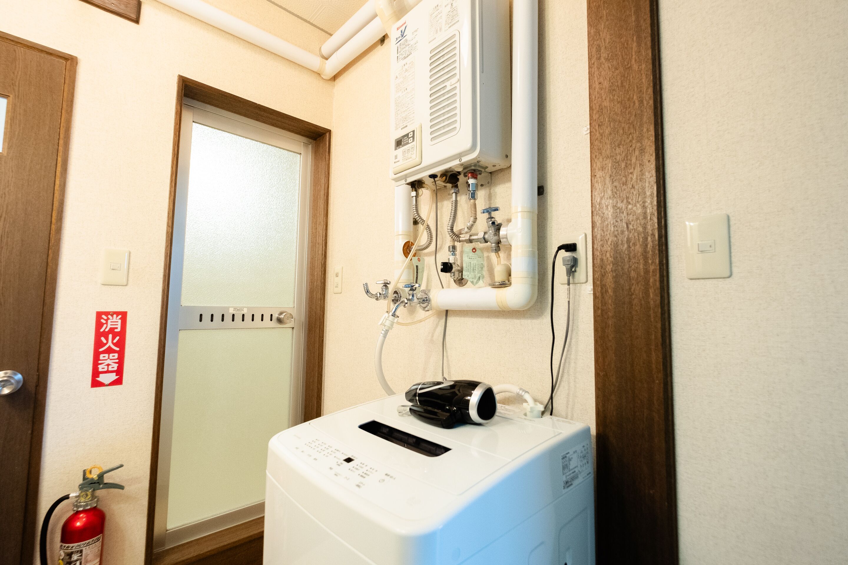 A laundry room with a white dryer, a fire extinguisher, and a water heater on the wall.