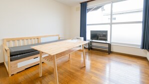 A room with a wooden floor, a wooden bench with a cushion, a wooden table, and a large window with curtains. - Furano Zone Ski Condo (Furano)