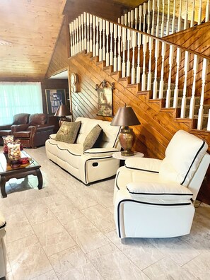 Una sala de estar con sofá, sillón, mesa de centro y una escalera con barandilla de madera.