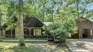 A cabin with a covered porch, surrounded by trees and a grassy area. - Cozy Country Home 3BR 3BA, 3200 sq. ft. will make your stay truly unforgettable! (Lufkin)