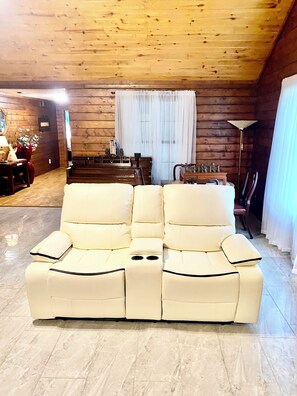A cozy living room with a cream-colored sofa, wooden walls, a dining area, and a floor lamp.