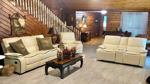 A spacious living area with a wooden staircase, two white leather sofas, a coffee table, and a chandelier. - Cozy Country Home 3BR 3BA, 3200 sq. ft. will make your stay truly unforgettable! (Lufkin)