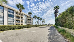 A multi-story hotel with balconies, a parking lot, and palm trees. - Fernandina Beach Paradise: Steps to Shore! (Fernandina Beach)