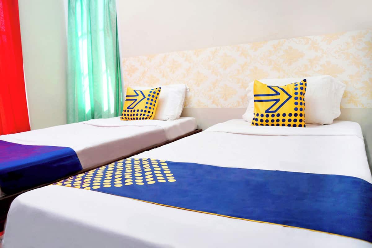 A hotel room with two beds, each with a white mattress and blue bedspread. There are decorative pillows with yellow and blue patterns.