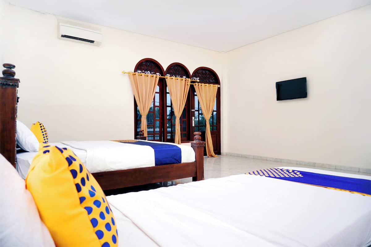 A hotel room with two beds, a flat-screen TV, and a window with curtains.