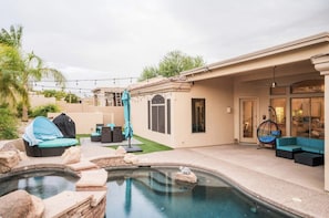 Un jardin avec une piscine, un espace salon extérieur et une terrasse couverte.