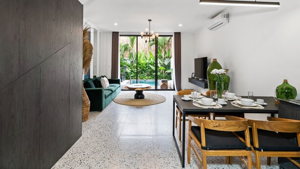 Una sala de estar moderna con un sofá verde, una mesa de comedor preparada para cuatro personas y vistas a una piscina a través de amplios ventanales.