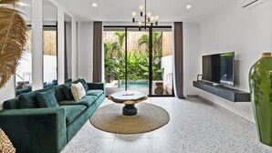Una sala de estar moderna con un sofá verde, una mesa de centro redonda y un televisor grande en la pared.