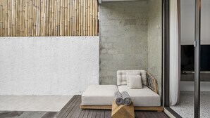 Un área de estar moderna al aire libre con un banco acolchado, un bloque de madera y toallas enrolladas.