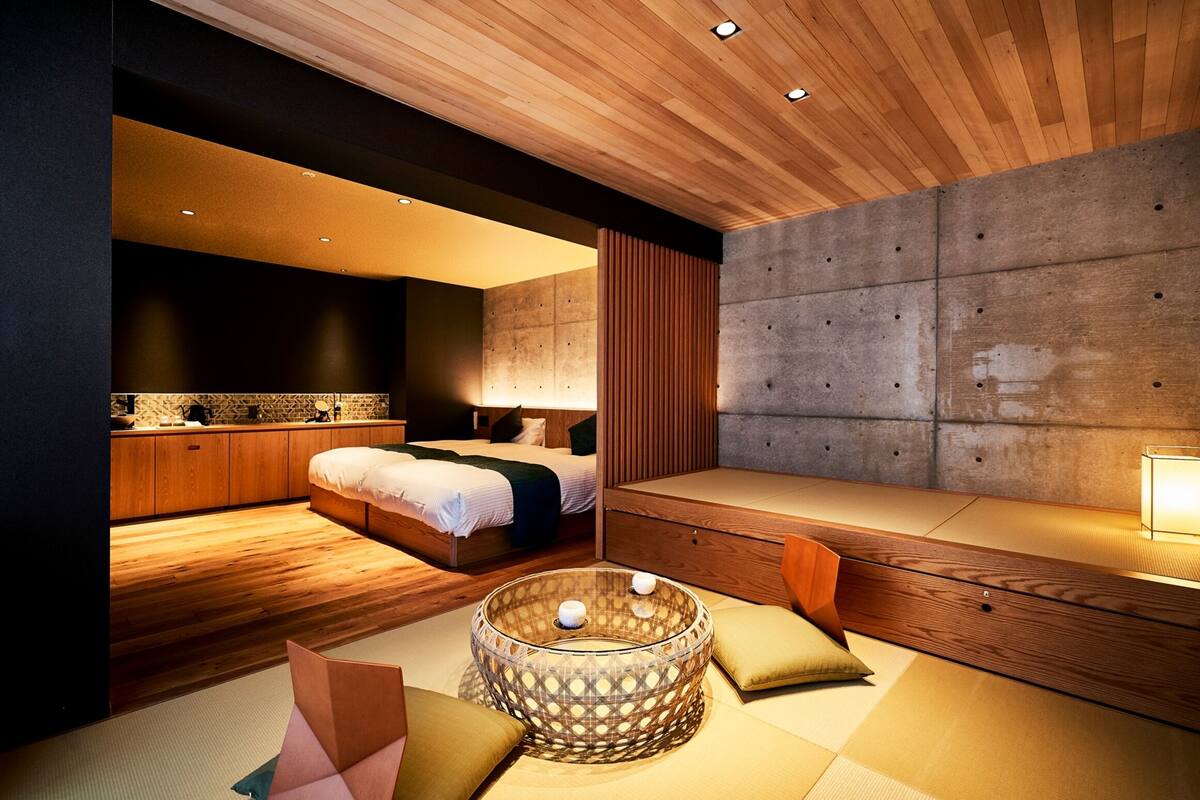 Une chambre moderne avec un plafond en bois, un grand lit, une table de chevet et un coin salon agrémenté de coussins.