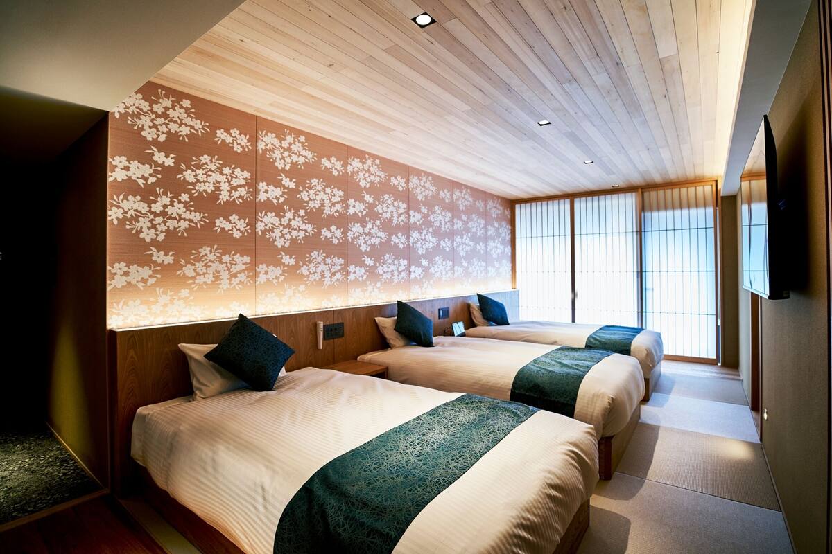 Une chambre d’hôtel avec deux lits, un plafond en bois et une grande fenêtre avec des stores.