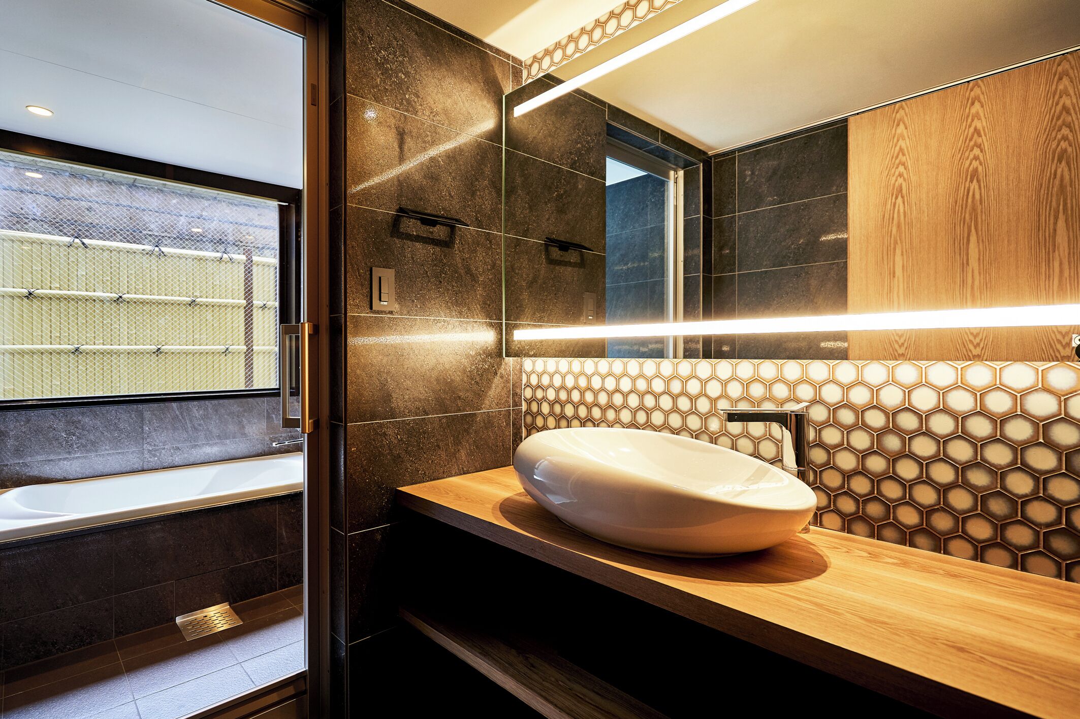 Un baño moderno con un espejo grande, un tocador de madera y una bañera.