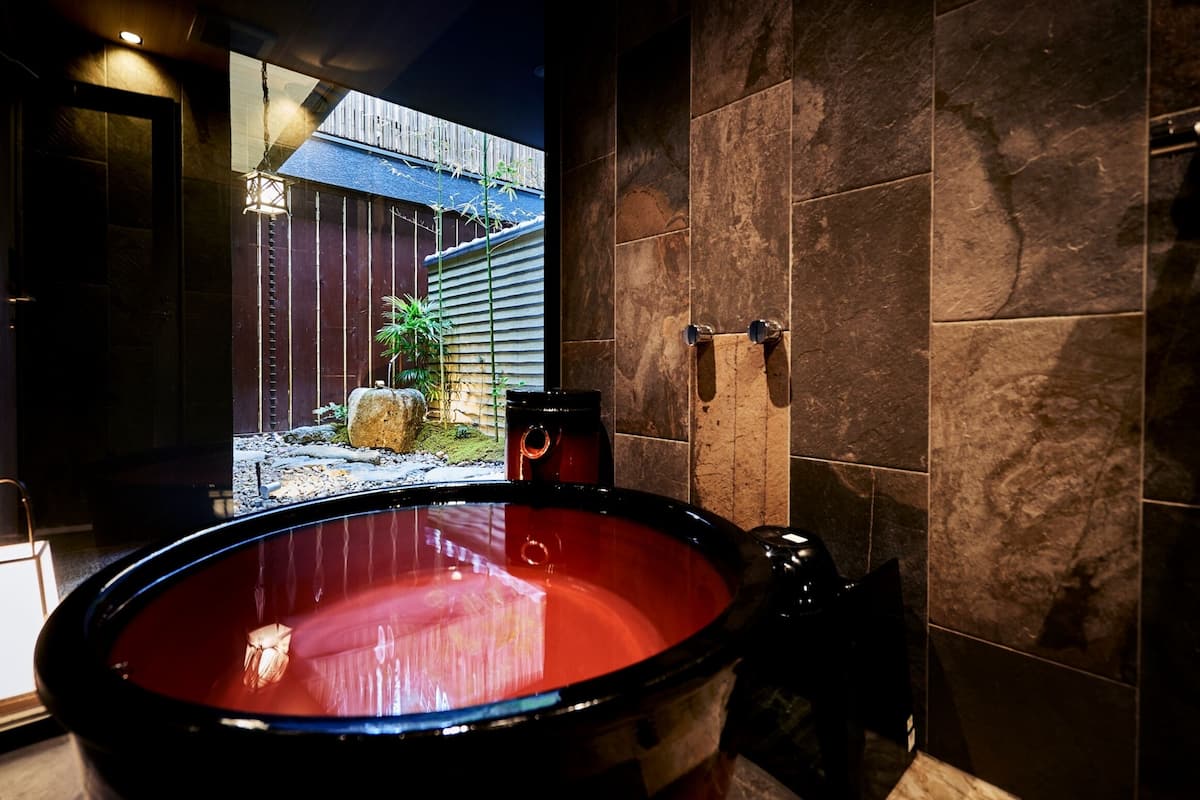 Un espace bien-être comprenant un grand bain à remous rouge, une clôture en bois et une vue sur un jardin de bambous.