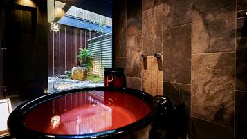 Un espacio de spa con un jacuzzi rojo grande, una valla de madera y vistas a un jardín de bambú.