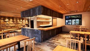 A restaurant with a stone wall, wooden ceiling, and a large window. Tables and chairs are arranged for dining. - kikokutei bekkan (Kyoto)