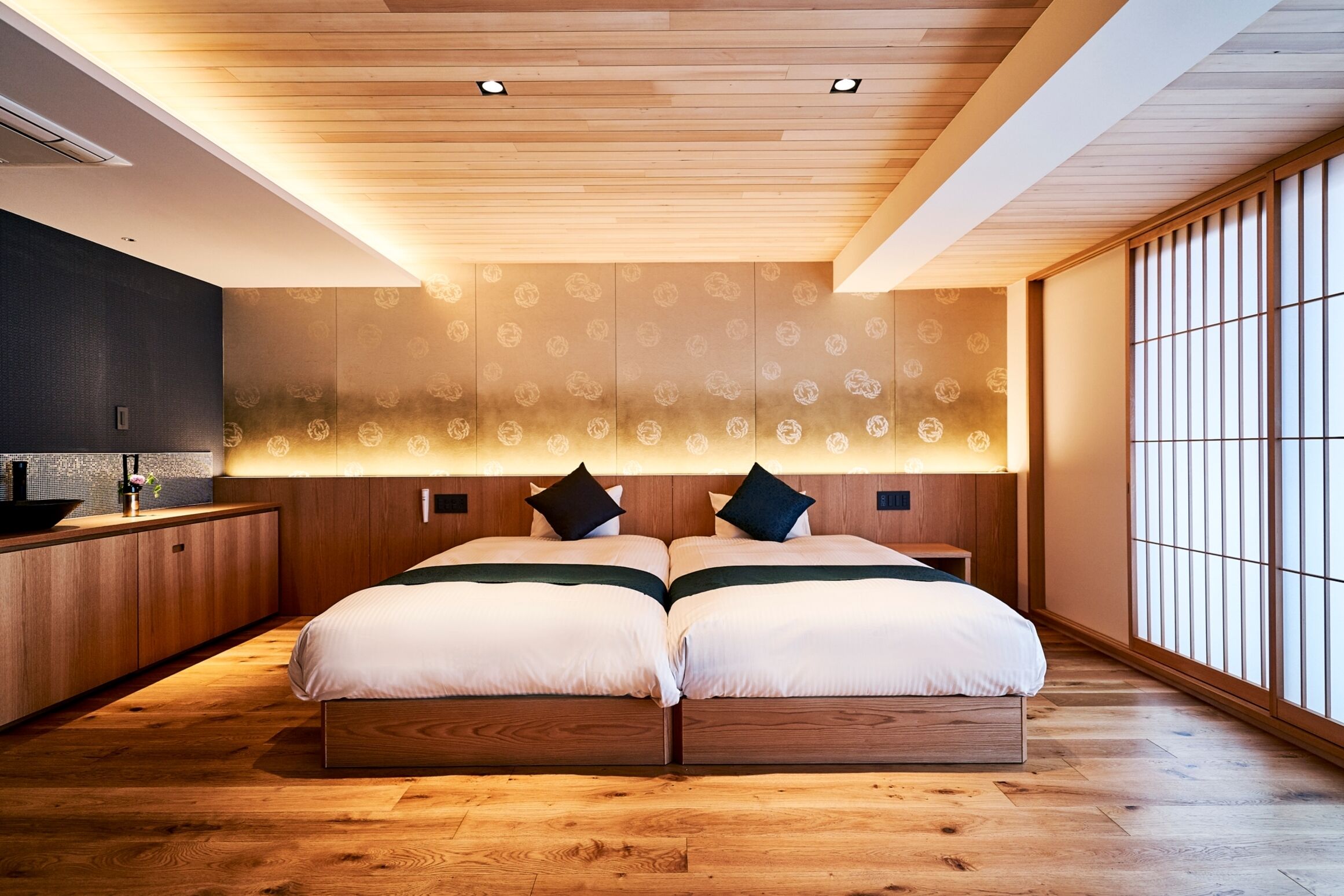 Un dormitorio moderno con techo de madera, una cama grande con dos almohadas, una mesita de noche y vistas a través de un panel shoji.