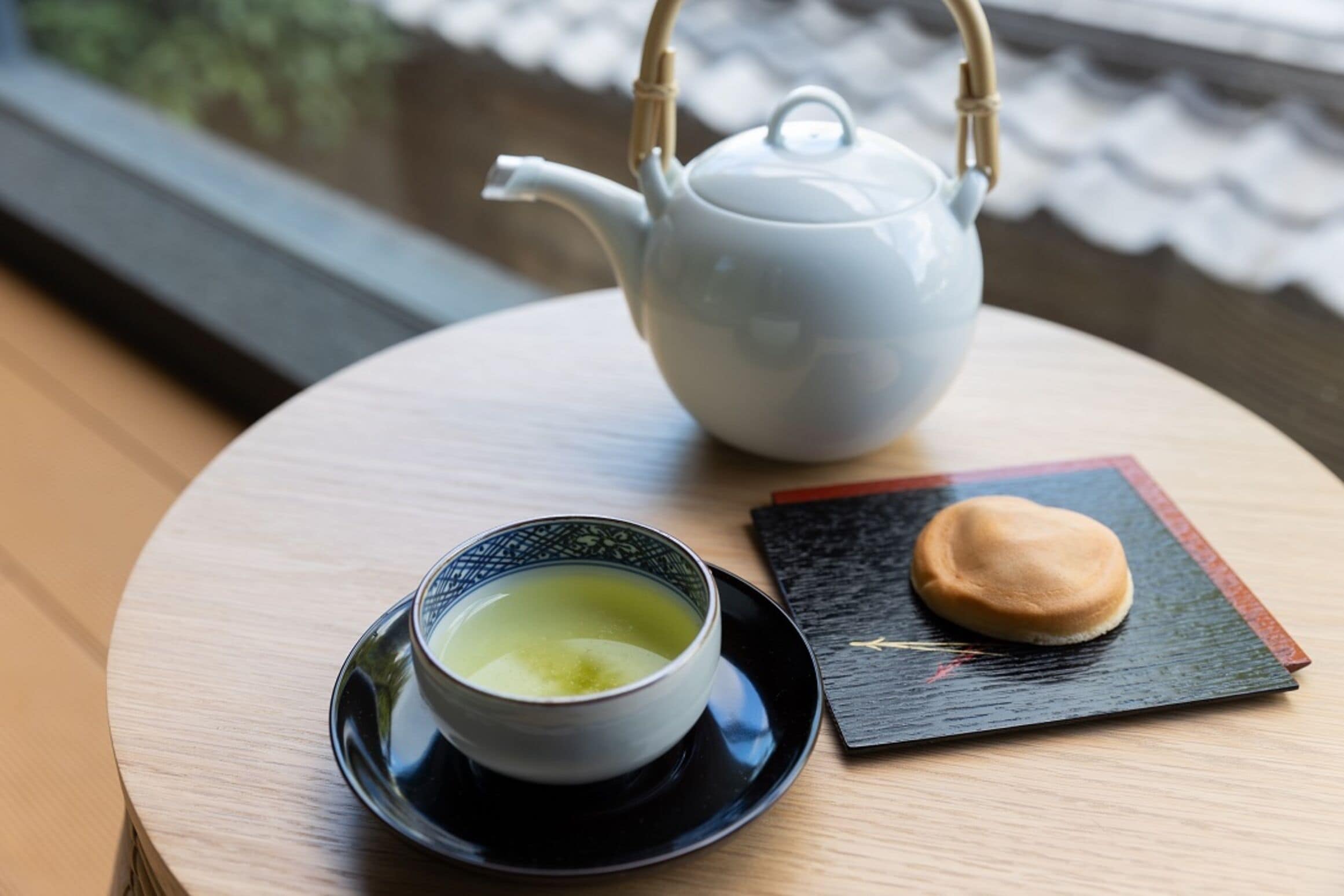 A round table with a white teapot, a cup of tea, and a small plate with a pastry.