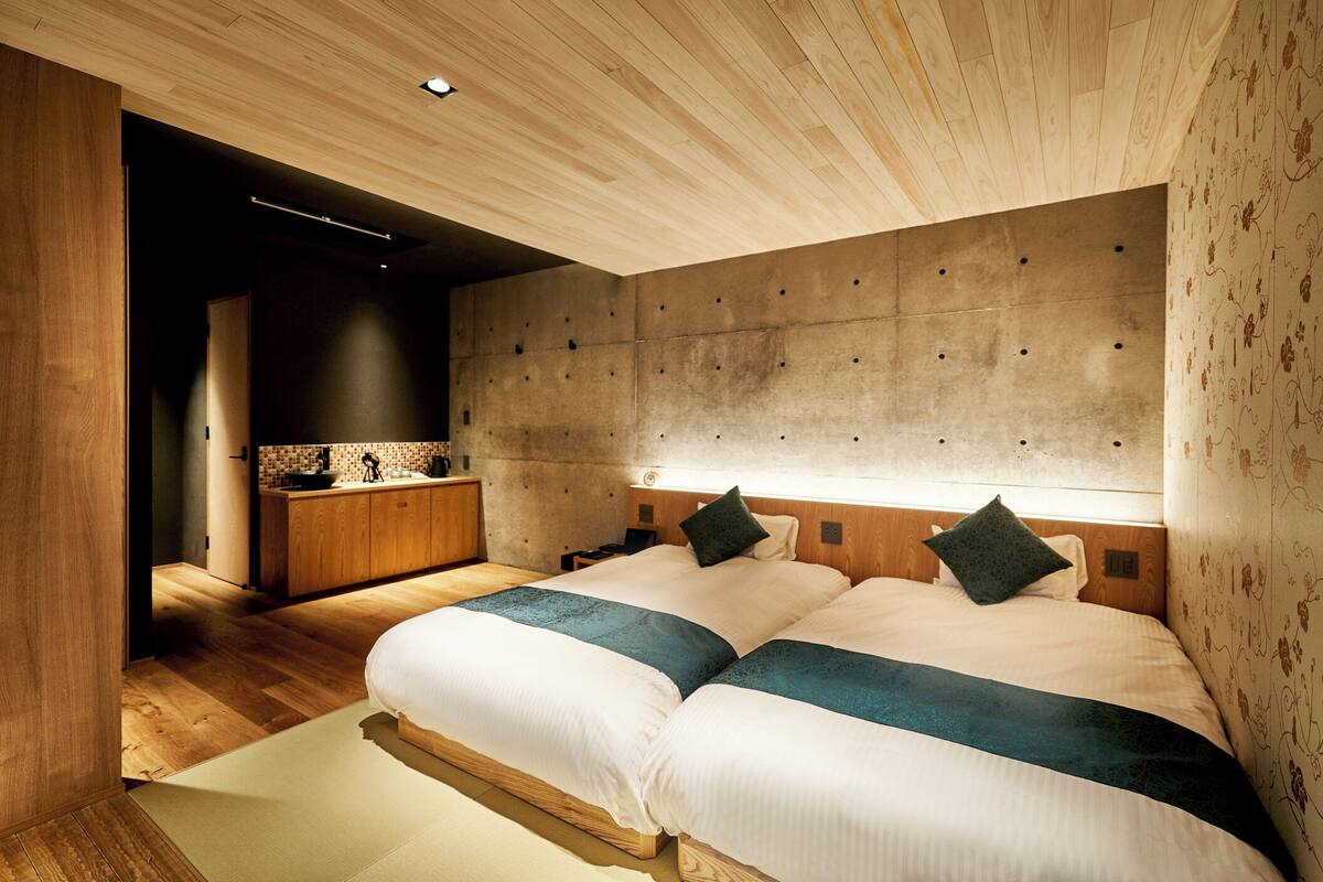 Une chambre moderne avec un grand lit, une tête de lit en bois et, au fond, une petite kitchenette.
