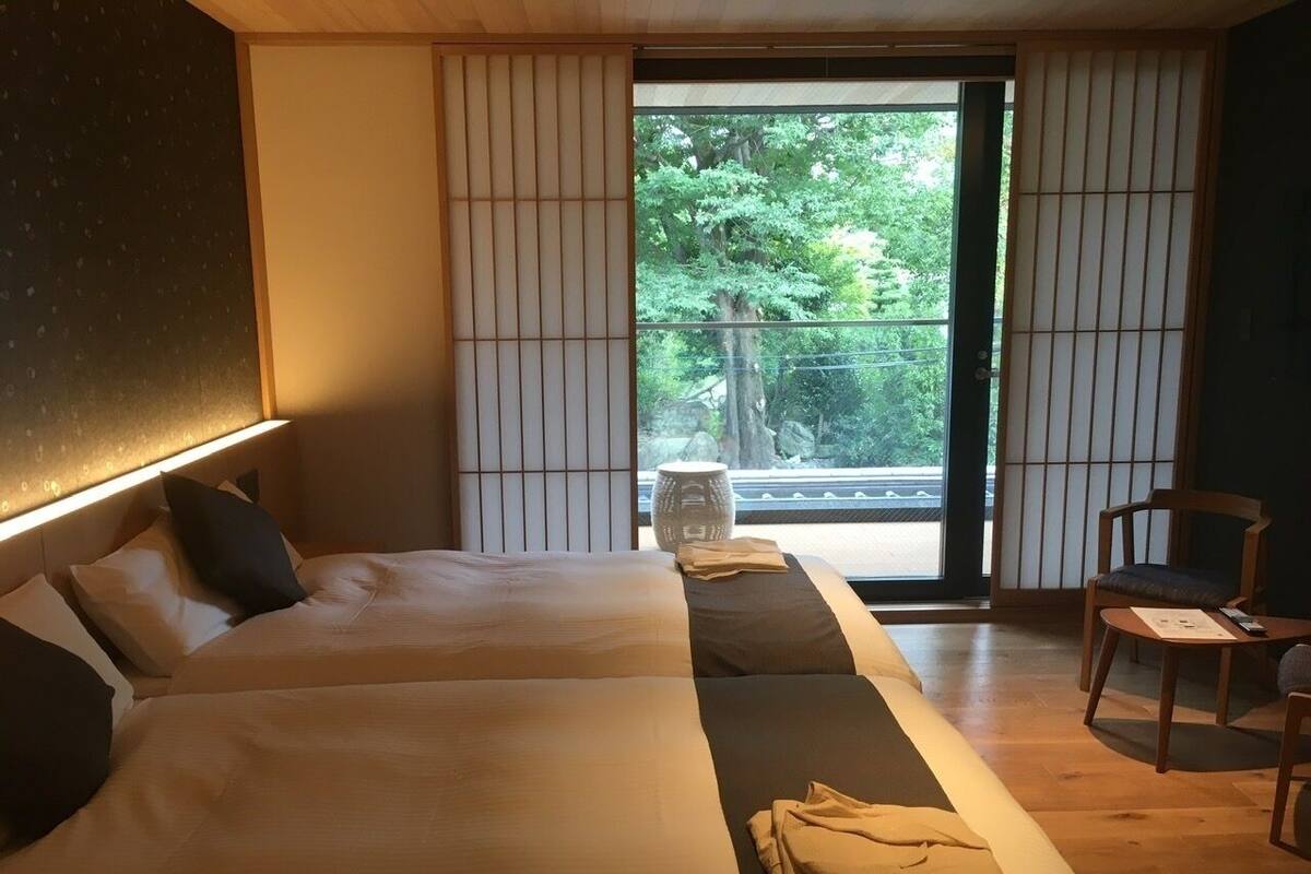 Une chambre d’hôtel avec deux lits, un plancher en bois, une porte-fenêtre coulissante donnant sur un balcon et une chaise.