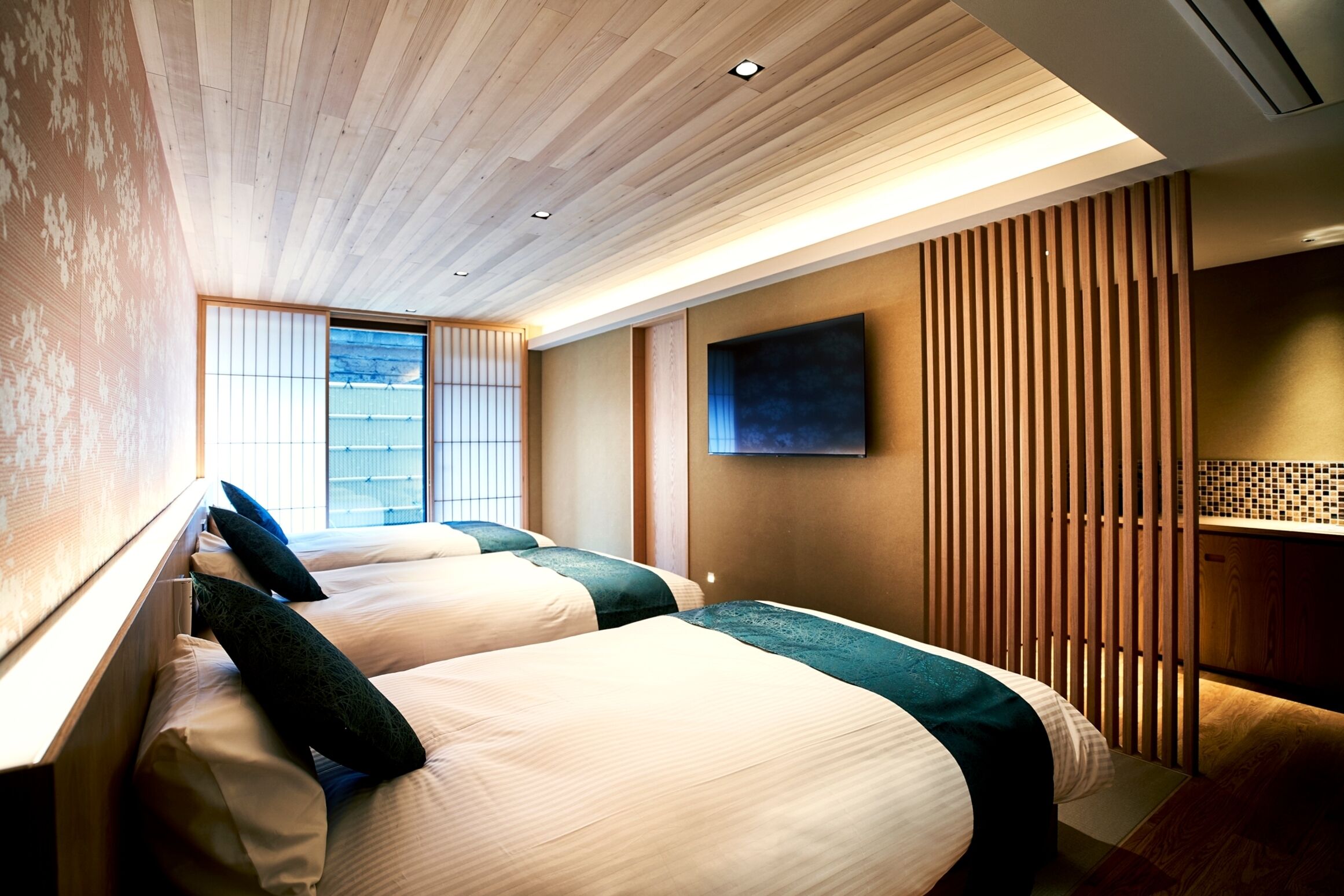 A hotel room with two beds, a wooden ceiling, a large window, and a television on the wall.