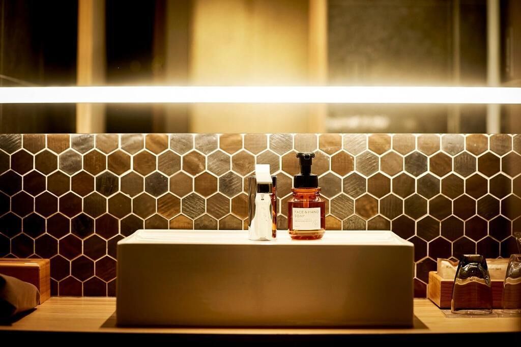 A bathroom with a rectangular sink, a soap dispenser, and a bottle of hand soap.