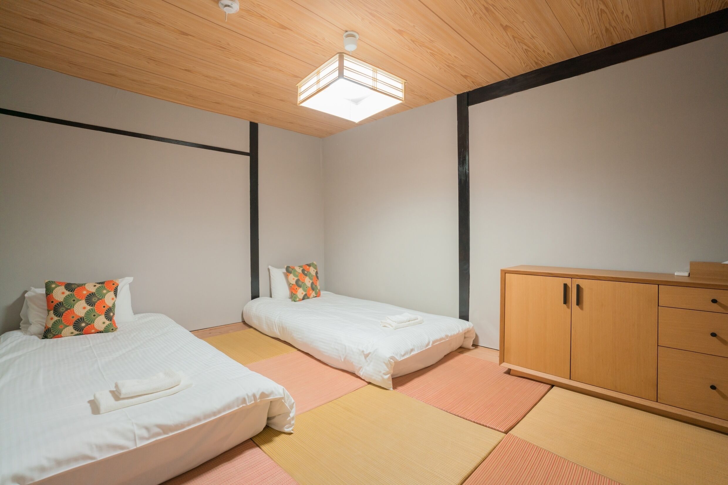 A room with two beds, a wooden cabinet, and a ceiling light fixture.