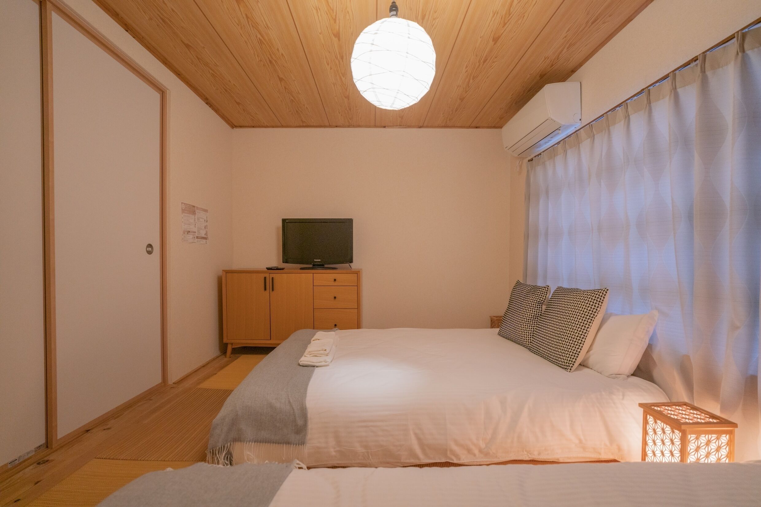 Une chambre à coucher avec un lit, un téléviseur posé sur une commode en bois et un luminaire au plafond.