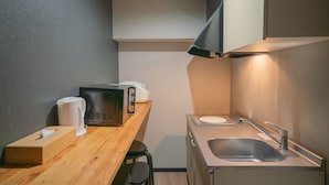 A compact kitchenette with a wooden countertop, a sink, a microwave, and a kettle. - Kujo Seisen (Kyoto)