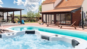 Een zwembad met een jacuzzi, buitenzitplaatsen en een overdekt terras.