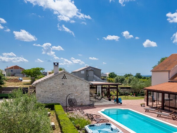 Ein Wohngebiet mit Schwimmbad, Steinhaus und überdachter Terrasse mit Gartenmöbeln.