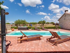 Ein Poolbereich mit zwei Holzliegen, einer Steinmauer und blauem Himmel.