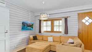 Una sala de estar acogedora con un sofá modular, un pequeño reposapiés, una lámpara colgante, una ventana con cortinas y un cuadro en la pared.