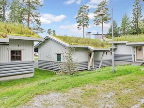 Een rij houten blokhutten met een grindpad ervoor, omgeven door groen en bomen.
