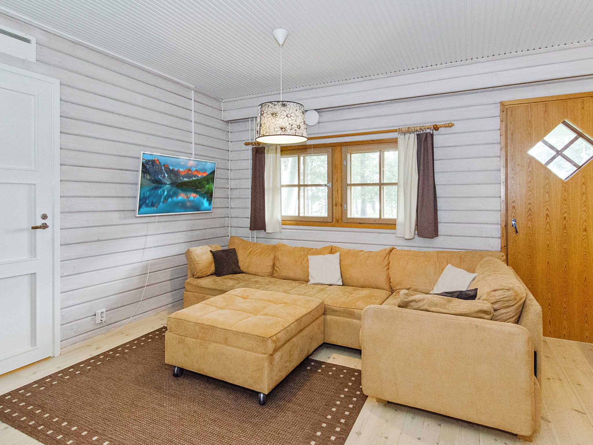 A room with a sectional sofa, a rug, a painting, and a window with curtains.