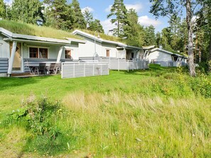 Een rij vakantiehuisjes met een gazon ervoor, omringd door bomen.