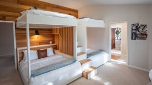 Une chambre avec deux lits superposés, un lambris en bois sur les murs, un escalier et une enseigne publicitaire pour la vente de glace et la location de matériel.