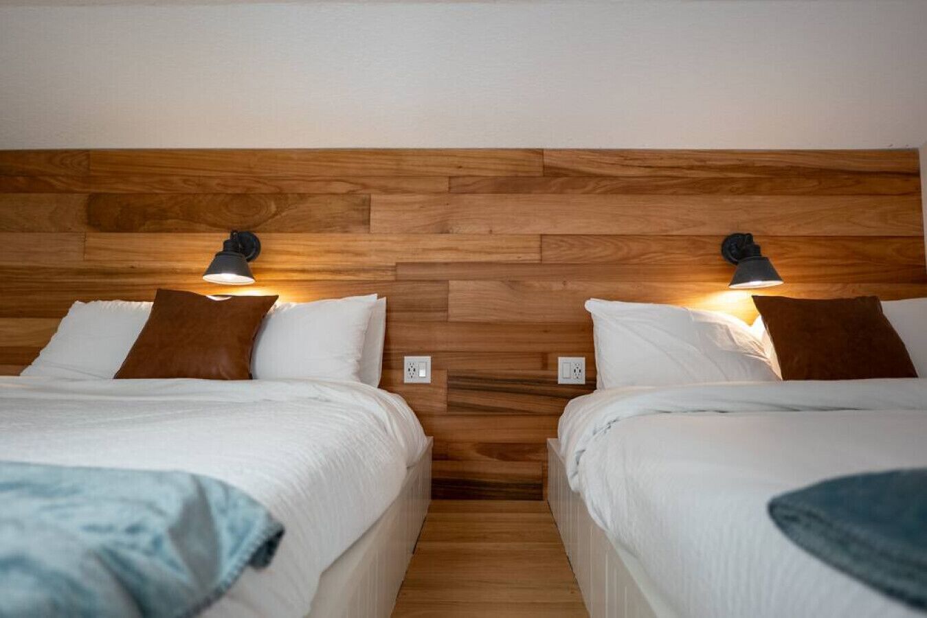 Een hotelkamer met twee bedden, een houten hoofdeinde, nachtlampjes en witte beddengoed.