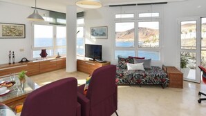 Sala de estar moderna com sofá, mesa de jantar e grandes janelas com vista para uma paisagem deslumbrante.