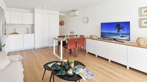 A modern, open-plan living space with a kitchen, dining area, and a TV displaying a beach scene. - Beachfront Nasas 4 JM by Interhome (San Agustín)